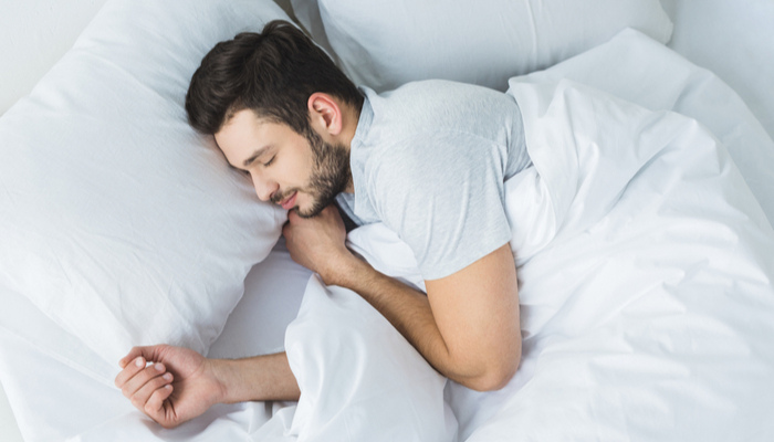 bearded man sleeping on bed with white sheet and pillows in bedroom