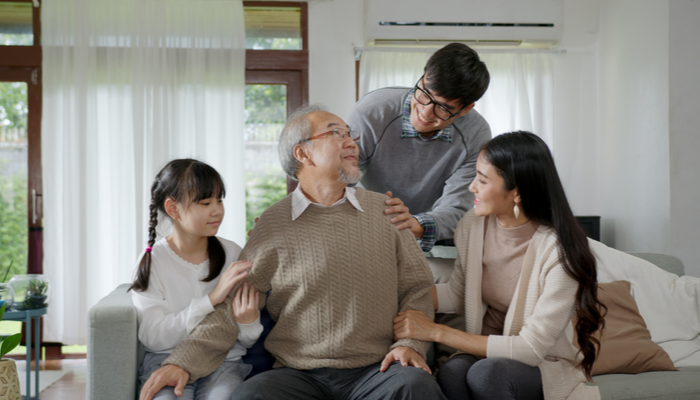 Asian elderly senior male with glasses sitting at sofa couch at home living room with chronic health issue with family