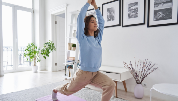 Fit healthy young woman in a blue sweater doing pilates yoga exercise fitness training workout at home interior standing in warrior pose.v