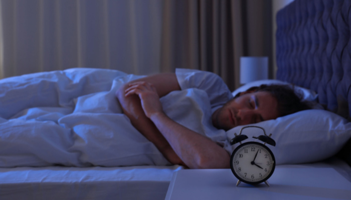 Alarm clock on nightstand near sleeping young man peacefully
