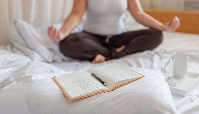 Mental health care, positive thinking and wellness concept. Woman lying in bed doing yoga, practicing stress relief challenge with journal about feeling