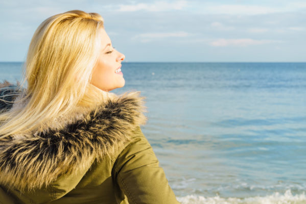 Blonde-Woman-wearing-warm-jacket-relaxing-on-beach-near-sea-cold-sunny-day-scaled